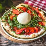 Pizza mit frischen Tomaten, Rucola und einer Kugel Burrata, die Lust auf burrata selber machen macht.