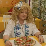 Kobieta z kręconymi włosami siedzi przy stoliku w bistro. Przed nią pizza, a za nią dekoracje ścienne. To idealne miejsce na bistro schadzka przy piecu.
