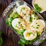 Jajka na twardo z sałatą, polane kremowym sosem majonezowo musztardowym, posypane szczypiorkiem i papryką.