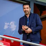 Gianluigi Buffon, legendarny włoski bramkarz, w eleganckim granatowym garniturze, obserwuje mecz z trybun.