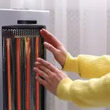 Manos cerca de un calentador eléctrico encendido. Las estufas eléctricas son peligrosas, ¡mantén la distancia!