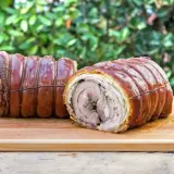Dwa pieczone kawałki porchetta, zawinięte w skórkę i sznurki, leżą na desce. To pyszne danie, które warto poznać!