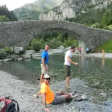 Gente disfrutando del río bajo el puente de piedra en Bujaruelo, con vistas al Taillón.