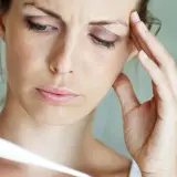 Frau mit Fieber, die sich die Stirn hält und ein Thermometer betrachtet. Psychosomatischer Fieber kann viele Ursachen haben.