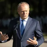 Donald Tusk w garniturze przemawia przy mikrofonie, gestykulując rękami.