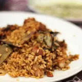 Deliciosa paella de conejo con trozos de carne dorada y verduras, servida en un plato blanco.