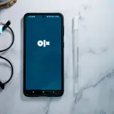 Telefon z aplikacją OLX, okulary i długopis na marmurowym tle. Dowiedz się, jak dodać ogłoszenie na OLX za darmo.