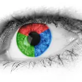 Occhio con iride divisa in settori rosso, verde e blu colore primario. Ciglia nere su sfondo bianco.