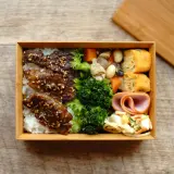 A delicious Japanese convenience store bento box filled with rice, teriyaki beef, broccoli, tamagoyaki, ham, and salad.