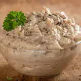 Pyszna pasta z tuńczyka, doprawiona pieprzem i udekorowana natką pietruszki, w szklanej miseczce na drewnianym tle.