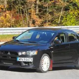 Czarny Mitsubishi Lancer 9 z białymi felgami i czerwonymi chlapacami na tle jesiennego lasu.