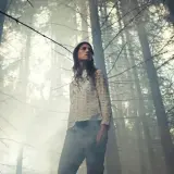 Una giovane donna in una foresta nebbiosa, con un'espressione pensierosa. Potrebbe essere una scena che evoca un' antichrist spiegazione, un'oscura profezia che si manifesta.