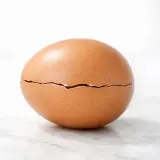 Un œuf brun craquelé, révélant un œuf noir à l'intérieur, sur fond clair.