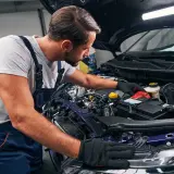 Mechanik w warsztacie dokonuje odsiarczania akumulatora w samochodzie, pracując przy otwartej masce.