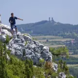 Trzech turystów na skale w Górach Świętokrzyskich, jeden wskazuje kierunek. W oddali ruiny zamku.