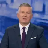 Mężczyzna w garniturze, prowadzący tvn wiadomości, z uwagą przekazuje informacje.