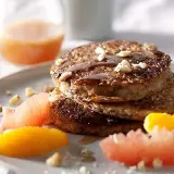 Pile de pancakes muesli, nappés de sirop et garnis de noix, accompagnés de quartiers d'agrumes.