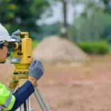 Geodeta w kasku i kamizelce odblaskowej pracuje z tachimetrem. Zastanawiasz się, ile kosztuje geodeta?