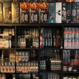 Półki pełne pudełek z grami i figurkami, w tym wiele z serii Warhammer. Widać tu zapowiedź przygód Gotreka i Felixa, a także inne tytuły.
