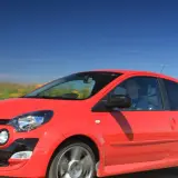 Czerwone Twingo RS pędzi przez kwitnące pola pod błękitnym niebem.