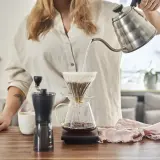 Kobieta przygotowuje kawę metodą v60 drip. Gorąca woda powoli przelewa się przez zmielone ziarna do dzbanka.