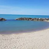 Spiaggia di Marina di Pisa con acque calme e dighe frangiflutti in pietra.
