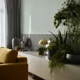 Szare ściany z czym łączyć? Wnętrze z żółtymi kanapami, roślinami i nowoczesną komodzą.