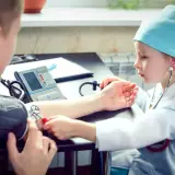 Dziecko w stroju lekarza mierzy ciśnienie. Czy tauryna podnosi ciśnienie? To pytanie, na które odpowiedzi szukają mali medycy.