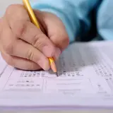 Dłoń z ołówkiem zaznacza odpowiedzi na arkuszu testowym. Przygotowanie do kursu CKZ.