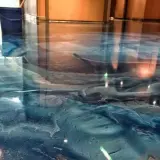 Błękitna żywica w garażu tworzy efekt fal oceanu. Widać niebieskie wiadro i odbicia światła.