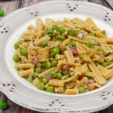 Un piatto di pasta con piselli, pancetta e pepe nero, servito su un piatto rustico.