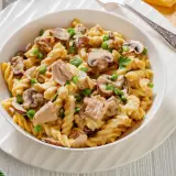 Makaron fusilli z tuńczykiem, groszkiem i pieczarkami w kremowym sosie, udekorowany natką pietruszki.