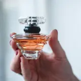 Dłoń trzyma flakonik perfum o bursztynowym kolorze, przypominający Baccarat Rouge.