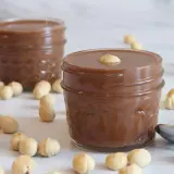 Dos tarros de deliciosa nutella vegana rodeados de avellanas. Una cucharilla plateada descansa cerca.