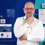 Mężczyzna w okularach zastanawia się nad danymi e-commerce. Widoczne są wykresy sprzedaży, zamówień i klientów, a także produkty. Paypo weryfikacja jest kluczowa dla analizy.