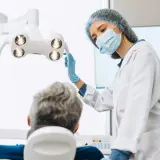 Dentystka w masce i rękawiczkach przygotowuje się do zabiegu. Pacjent siedzi na fotelu. Czy dentysta może wystawić L4?