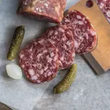 Plasterki salami z widocznym tłuszczem, ogórki konserwowe i cebulka. Salami jest z mięsa wieprzowego i wołowego.