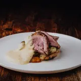 Tranches de gigot d'agneau au four, nappées d'une sauce crémeuse, servies sur des pommes de terre rôties. Un délice visuel et gustatif.