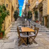 Malta sierpień: kamienne schody i stoliki kawiarniane w wąskiej uliczce, idealne na letni wieczór.