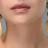 Labios maquillados y pendientes dorados con detalles que recuerdan a tipos de piedras preciosas.