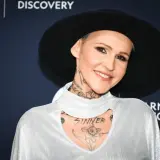 Agnieszka Chylińska w białej bluzce i czarnym kapeluszu, z widocznymi tatuażami na szyi i klatce piersiowej.
