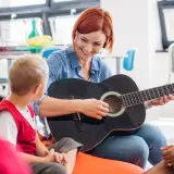 Nauczycielka gra na gitarze dla dzieci, tworząc zindywidualizowaną ścieżkę kształcenia. Przykłady takiej nauki to muzyka.