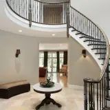 Elegancka, zakręcona klatka schodowa z ciemnego drewna i czarnymi balustradami dominuje w przestronnym holu.