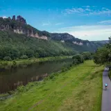 Rowerzysta przemierza malowniczą ścieżkę wzdłuż rzeki, podziwiając skaliste klify i zielone lasy. To piękny zakątek Szwajcarii Czeskiej.
