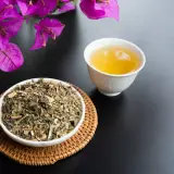 Una tazza di tisana per digerire accanto a una ciotola di erbe secche, con fiori viola sullo sfondo.