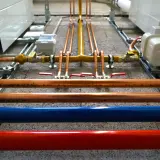Instalacja hydrauliczna z miedzianymi rurami, zaworami i niebieską/czerwoną rurą. Ocieplenie rury wodnej jest kluczowe dla efektywności systemu.