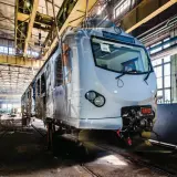 Nowy pociąg EN57 przechodzi modernizację w hali produkcyjnej. Widać jego front i część wagonu.