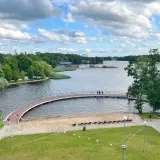 Malownicze jezioro w Szczecinku z łukowatym mostkiem, piaszczystą plażą i zielonymi terenami rekreacyjnymi.