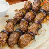 Grillowane szaszłyki z mielonego mięsa i bakłażana, czyli pyszna kofta libańska, podane na chlebku z sosem.