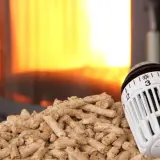 Holzpellets vor einem Kaminfeuer, daneben ein Thermostat zur CO2-Steuer.